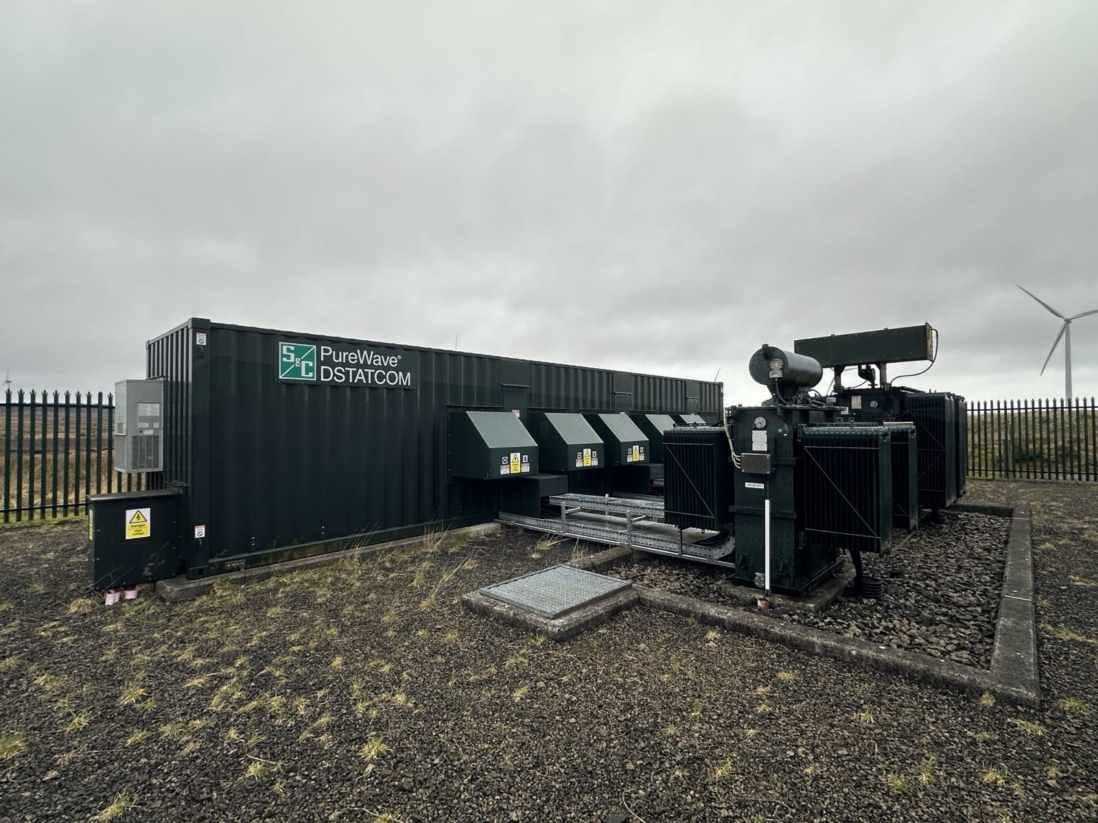 PureWave DSTATCOM and transformer installed at a wind farm substation, with a turbine behind